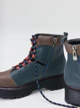 Botas de cuero estilo trekking, en combinación de colores verde, marrón y gris, con plataforma de goma negra, cordones bicolor inspirados en cuerdas de escalada y pasadores en tono rojizo.