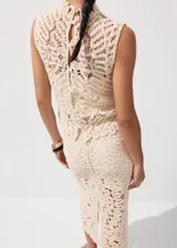 Top de tejido calado color beige, con cuello halter, sin mangas y cierre de botones en la espalda.