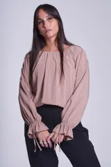 Blusa de manga larga color rosado, con cuello redondo y puños elásticos con volados y lazos decorativos. Presenta un diseño holgado con frunces en el escote.