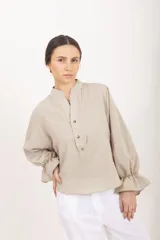 Blusa de diseño cuadrillé en tonos beige y verde claro, de corte amplio y mangas largas abullonadas con puños elastizados con volados. Cuenta con cuello mao y una abertura frontal parcial con botones.