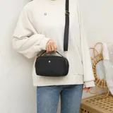 Cartera bandolera negra de lona, con cierre de cremallera, herrajes dorados y correa ajustable.