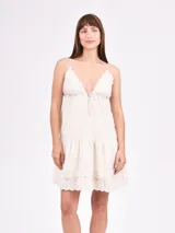Vestido corto de tirantes finos con escote en V, confeccionado en tela con detalles de bordado inglés en el escote y el ruedo. Presenta un corte debajo del busto con cordón ajustable y falda con volado.