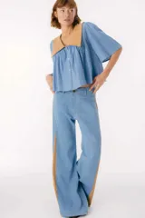 Pantalón de jean azul oscuro de pierna ancha y tiro medio, con paneles laterales en contraste de color marrón. Presenta costuras pespunteadas en tono tostado y terminación desmechada en el bajo.