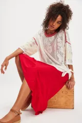 Remera oversize de inspiración deportiva en malla de encaje color blanco, con terminaciones en rojo, franjas estilo varsity en las mangas, escote redondo, hombros caídos y aberturas laterales en el ruedo.