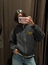 Hoodie canguro con cierre frontal, color negro con efecto acid wash, con capucha y bolsillos tipo canguro. Presenta el texto estampado en amarillo "Now You Do What They Told Ya" en el pecho.