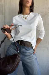 Remera de manga larga color blanco, con cuello redondo y detalle de tachas metálicas en los hombros.