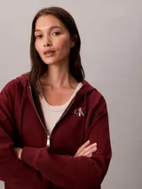 Campera canguro Calvin Klein de felpa color bordó, con capucha ajustable por cordones, cierre frontal completo de cremallera, mangas largas y bolsillos laterales. Presenta el logo monograma de la marca bordado en el pecho.
