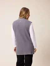 Chaleco de tejido de punto en color gris, con cierre frontal completo, cuello alto y dos bolsillos delanteros tipo parche.