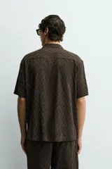 Camisa de corte relajado con cuello bowling y manga corta. Confeccionada en tejido fluido con textura jacquard de patrón geométrico y cierre frontal de botones.
