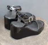 Sandalias negras de charol con plataforma y taco de cuña. Tira ancha sobre los dedos y pulsera con hebilla al tobillo.