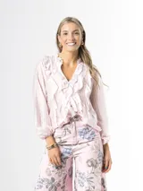 Camisa de organdí rosa pastel con finas rayas verticales metalizadas, escote en V con volados frontales y mangas largas abullonadas con puños elásticos.