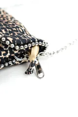 Cartera bandolera pequeña con estampado animal print tipo leopardo, solapa frontal y correa combinada de eslabones metálicos plateados y sección superior en el mismo estampado.