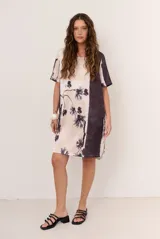 Vestido corto de corte recto y holgado, con mangas cortas y cuello redondo. Presenta un diseño estampado con motivos florales oscuros y una franja lateral en tono contrastante.