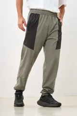 Pantalón deportivo gris con paneles laterales negros, cintura elástica y puños ajustados.