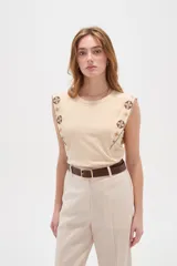 Remera de algodón color beige, sin mangas, al cuerpo y con cuello a la base. Presenta detalles bordados en los hombros con diseños geométricos.
