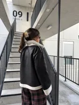 Campera tipo gamulán de cuero sintético negro con interior y detalles de corderito blanco. Presenta cierre frontal, bolsillos laterales y diseño holgado.