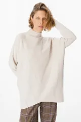 Sweater de punto color beige, con cuello alto acanalado, mangas largas y diseño holgado. Presenta un patrón de costuras verticales que forman un diseño de espiga en el frente.