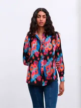Camisa de manga larga con estampado floral multicolor sobre fondo negro, cuello clásico y cierre frontal de botones.