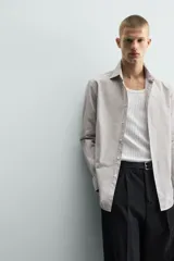 Camisa de corte slim fit confeccionada en tejido de algodón, con estampado de cuadros pequeños en tonos beige y blanco. Presenta cuello italiano, manga larga con puños abotonados y cierre frontal con botones.