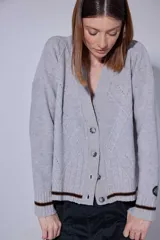 Saco tejido de punto en lambswool, con diseño de rombos y detalles de aranes en el frente. Presenta cierre frontal con botones jaspeados y puños con franjas en contraste. Incluye detalle de pin bordado en la manga.