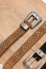 Cinturón de cuero gamuzado color camel, con diseño de tachas metálicas plateadas dispuestas en grupos triangulares y hebilla metálica labrada de estilo western.