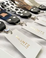 Llavero de tela con estampado animal print en tonos verde, negro y beige. Tiene un mosquetón metálico plateado y detalles en cuero sintético negro.