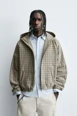 Cazadora boxy fit de algodón con estampado de cuadros en tonos beige y gris. Presenta cuello con capucha, cierre frontal de cremallera, mangas largas con puños elásticos y bolsillos frontales tipo canguro.