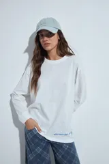 Remera de manga larga en color blanco, con corte relajado y cuello redondo. Presenta un pequeño estampado gráfico en la parte inferior frontal con la frase 'WHO WH WHO?' y un dibujo de un perro.
