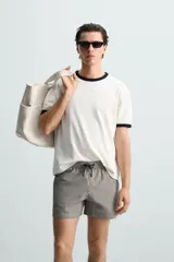 Bañador de hombre color verde claro con finas rayas blancas verticales (efecto seersucker). Tiene cintura elástica ajustable con cordón verde, bolsillos laterales y un bolsillo trasero de vivo.