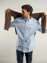 Camisa de corte regular confeccionada en algodón, con diseño de rayas verticales en tonos azul y blanco. Presenta cuello con botones, cierre frontal abotonado, bolsillo en el pecho con logo bordado y mangas largas.