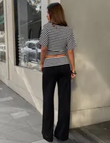Conjunto compuesto por un top cropped de rayas blancas y negras, con escote en V y mangas cortas, y un pantalón largo negro de pierna ancha con cintura baja y detalle de rayas a juego.