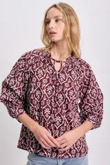 Blusa de estilo boho color bordó con estampado floral blanco, cuello redondo con cordones ajustables y mangas largas abullonadas con puños elásticos.