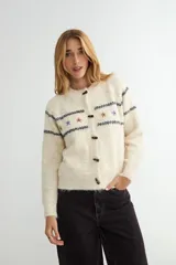 Cardigan de punto gris con cierre frontal de botones oscuros. Presenta un diseño de rayas horizontales oscuras y pequeños bordados florales en la parte superior del pecho y mangas.