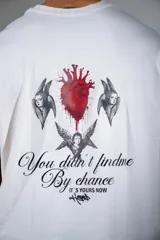 Remera de corte oversize color blanco, con cuello redondo y mangas cortas. Presenta un pequeño estampado gráfico central en el pecho con diseño de querubín con alas.