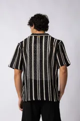 Camisa de manga corta tejida al crochet con diseño de rayas verticales negras sobre una base color crudo. Presenta cuello solapa y cierre frontal con botones.