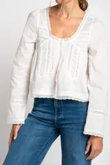 Blusa blanca de algodón con escote en U y mangas largas acampanadas. Presenta detalles de encaje en el escote, el frente y los puños.