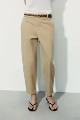 Pantalón chino color beige de tiro medio con bolsillos frontales y falsos bolsillos de vivo en la espalda. El bajo tiene un acabado con vuelta. Incluye un cinturón trenzado marrón.