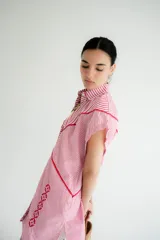 Vestido camisero corto blanco de algodón con bordados negros, cuello camisero, cierre frontal con botones y sin mangas.