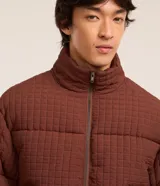 Campera marrón de poliamida con textura cuadriculada, corte boxy, cuello alto, cierre frontal con cremallera, bolsillos laterales y puños elásticos.