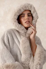 Capa de piel sintética en color negro, con diseño holgado, capucha integrada y bordes con textura de pelo largo.