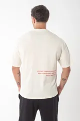 Remera de corte oversize color beige con estampa de texto en color rojo en la parte inferior trasera.
