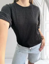 Blusa negra de manga corta con cuello redondo y textura tipo nido de abeja o gofrado en todo el tejido.