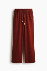 Pantalón de pierna recta en tejido liviano mezcla de lino y viscosa, color rojo. Cuenta con cintura elástica de tiro bajo, cordón de ajuste con cuentas decorativas en los extremos y bolsillos laterales al bies.