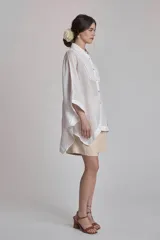 Camisa blanca de lino con cuello clásico, cierre frontal con botones, mangas anchas 3/4 y detalles de bordado calado en el canesú y los puños.