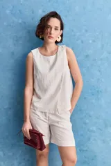 Top blanco sin mangas, con cuello redondo, diseño cruzado en el frente y cierre con botones en el hombro.