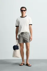 Bañador de hombre color verde claro con finas rayas blancas verticales (efecto seersucker). Tiene cintura elástica ajustable con cordón verde, bolsillos laterales y un bolsillo trasero de vivo.