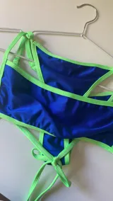 Bikini azul eléctrico con ribetes y tiras ajustables en verde neón. El corpiño es triangular y la bombacha es tipo vedetina con tiras laterales.