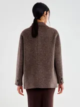 Chaqueta de paño gris de corte amplio, con solapas clásicas, cierre frontal cruzado de botones y bolsillos laterales con solapa.