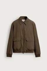 Cazadora regular fit de tejido técnico color marrón, con cuello solapa, manga larga y cierre frontal de cremallera. Presenta bolsillos de plastrón con solapa en la cadera y acabados con rib elástico.