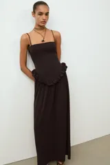 Vestido largo de color negro con escote recto y tirantes finos ajustables. Presenta un diseño con detalle de volante tipo peplum en la cintura y falda con caída fluida.